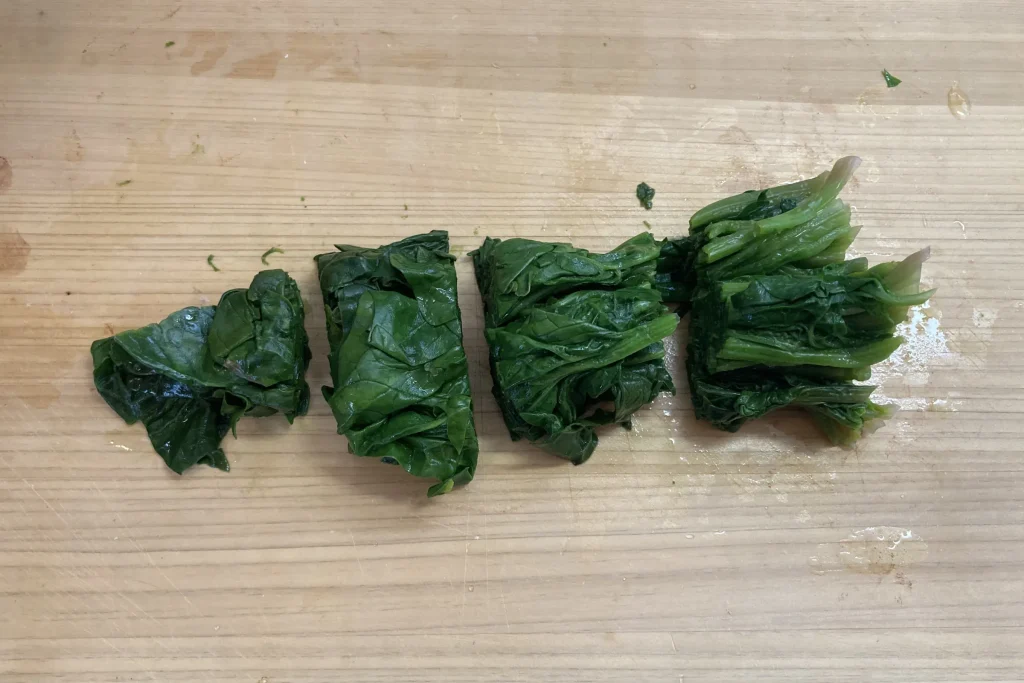 木製のまな板の上で、茹でたあとに水気を絞り、食べやすい大きさに4等分にカットされた鮮やかな緑色のほうれん草。