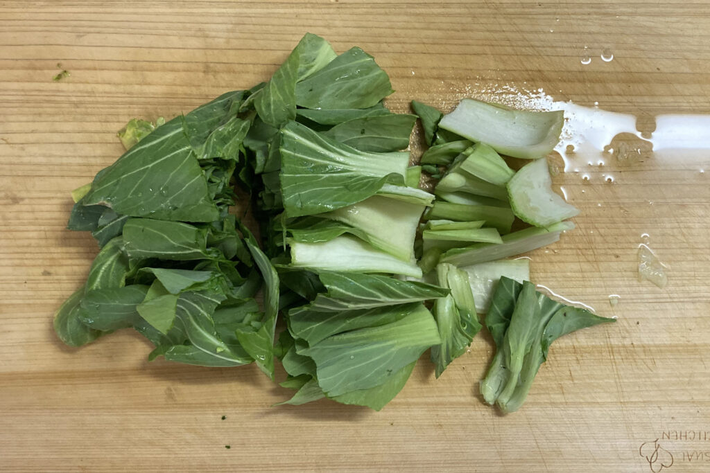 まな板の上でざく切りにしたチンゲン菜の下ごしらえ写真。白い茎と緑の葉が混ざった3cm幅のカット済みチンゲン菜がまな板に広がっている