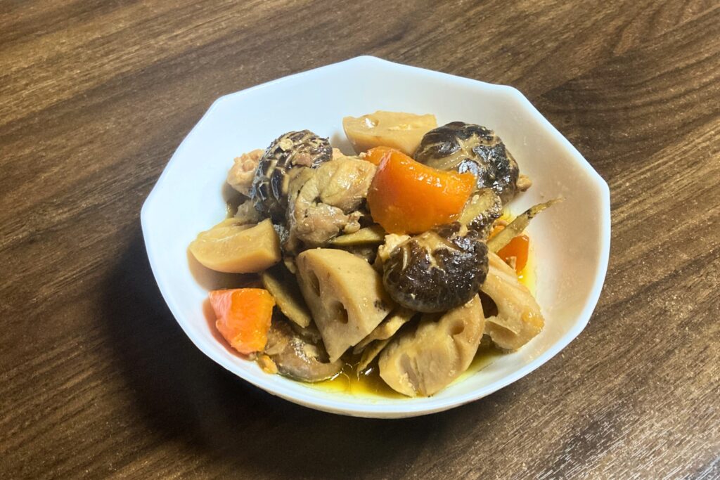 白い八角形の皿に盛り付けられた筑前煮。鶏肉、れんこん、にんじん、しいたけ、ごぼうが彩りよく配置されている。