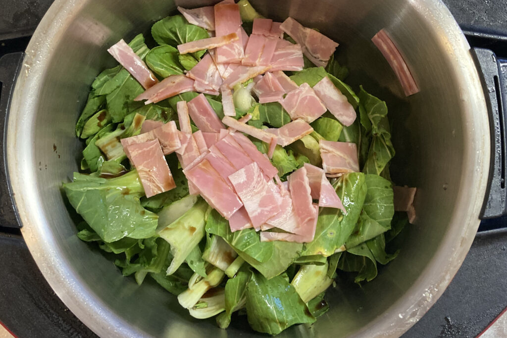 ホットクック内鍋にチンゲン菜とベーコンをセットした調理前の状態。緑のチンゲン菜の上にカットしたベーコンがのせられている