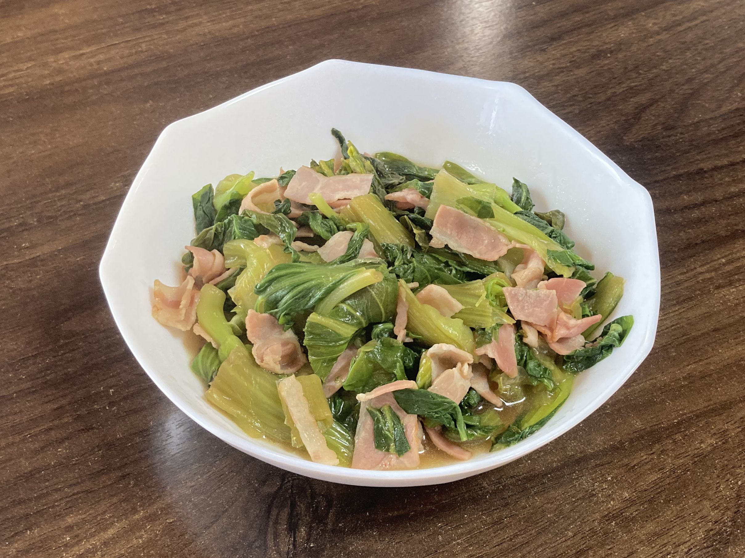 白い器に盛り付けられたホットクックで作ったチンゲン菜とベーコンのウスターソース炒め。しんなりとした緑のチンゲン菜とピンク色のベーコンが美しく絡み合っている