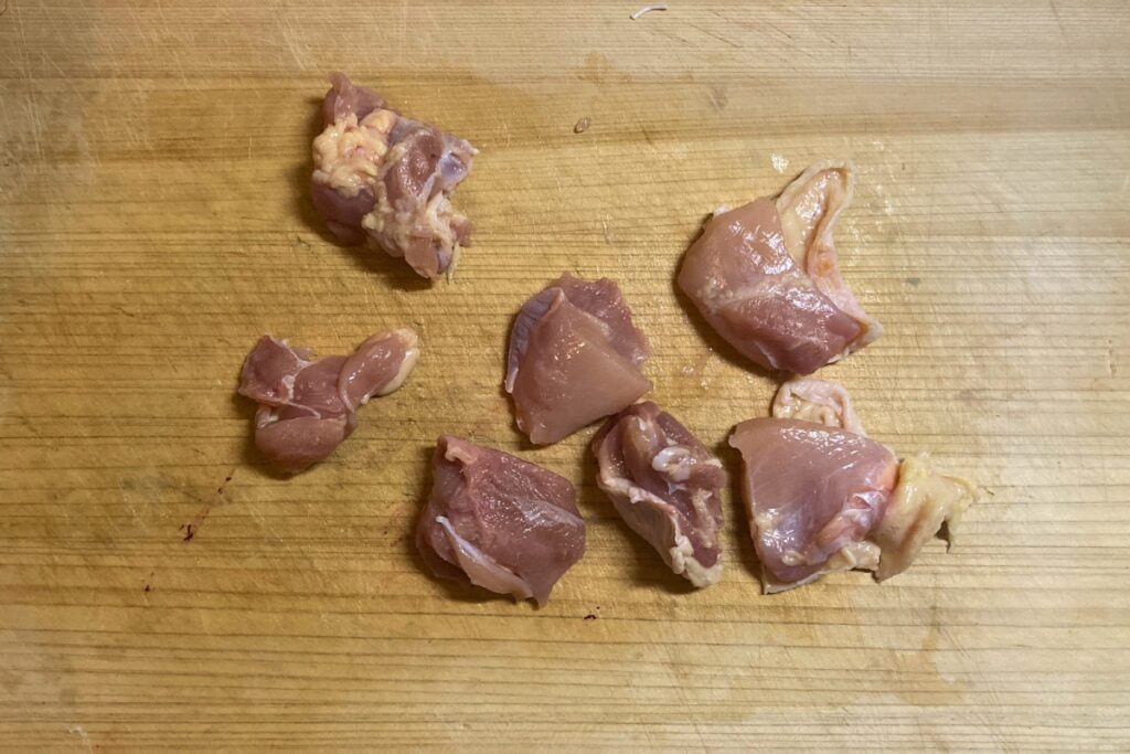 ホットクックで調理する前の下準備として、鶏もも肉を一口大（3〜4cm角）に切っている様子。大きめにカットすることで、加熱後もジューシーでパサつきにくい仕上がりになります。