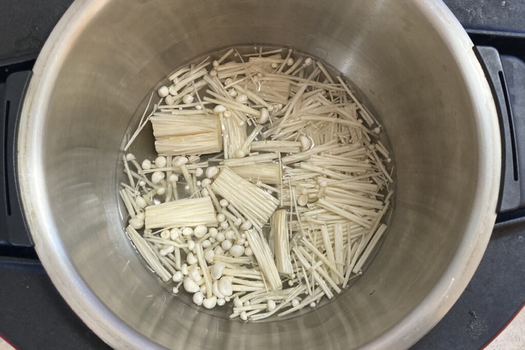 シャープの自動調理鍋ホットクックの内鍋に、食べやすい大きさにカットされた白いエノキタケが水に浸かっている様子。調理を開始する前の準備段階の俯瞰写真。