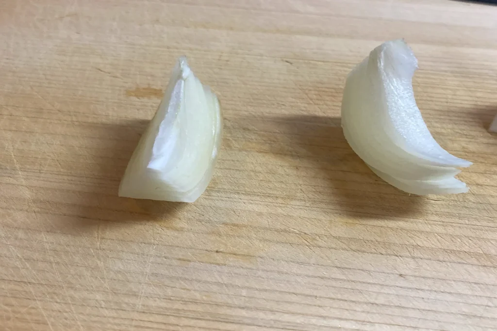 基本（推奨）: 木製のまな板の上に置かれた、くし形に切られた2つの玉ねぎ。根元を繋げたまま縦に等分された、料理の下準備段階の様子。