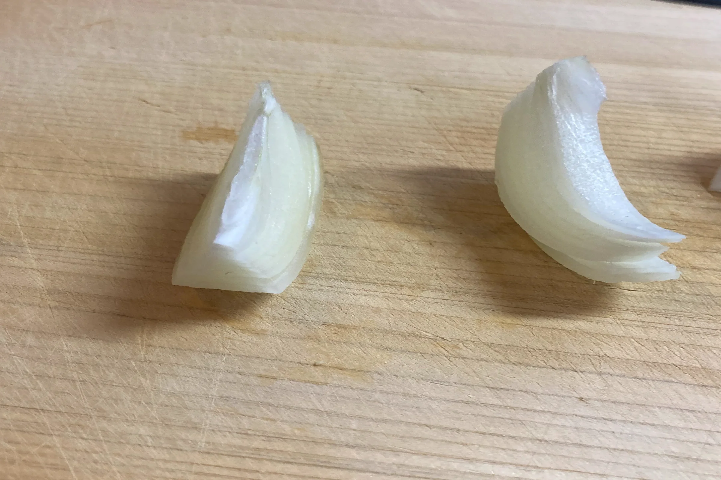 基本（推奨）: 木製のまな板の上に置かれた、くし形に切られた2つの玉ねぎ。根元を繋げたまま縦に等分された、料理の下準備段階の様子。