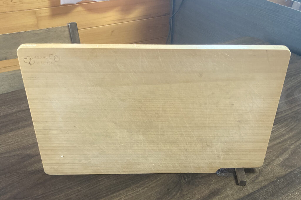 「CASUAL KITCHEN」の文字とハートの刻印が入った、長方形の木製カッティングボード。使い込まれた包丁の跡が表面に残っており、温かみのあるキッチンの雰囲気を伝える、立てかけられた状態のまな板の画像。