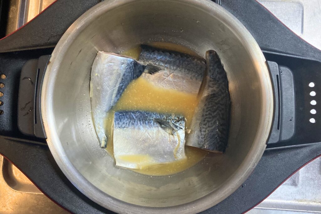 電気圧力鍋の内鍋に、生のサバの切り身が4切れと黄色い煮汁が入っており、調理を開始する前の状態。