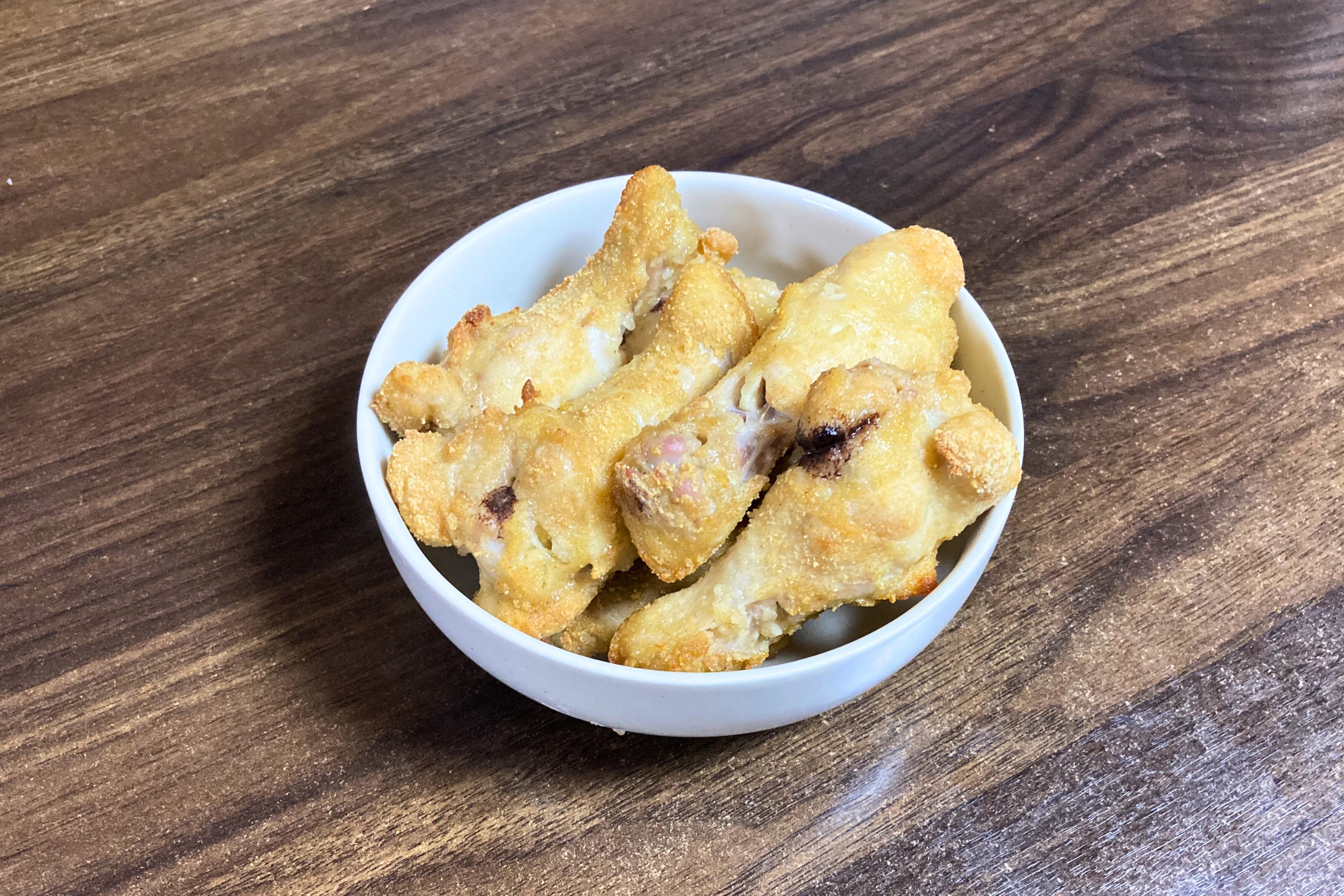 オーブンでキツネ色に香ばしく焼き上げられた鶏手羽元の唐揚げが、白い深めのボウルにこんもりと盛り付けられている様子。