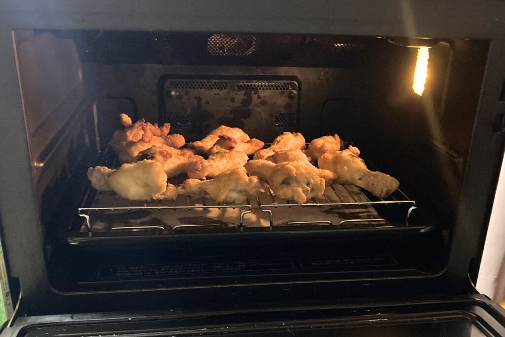 オーブンでの加熱が終わり、衣がこんがりと黄金色に焼き上がった熱々の鶏手羽元が庫内の網の上に乗っている様子。