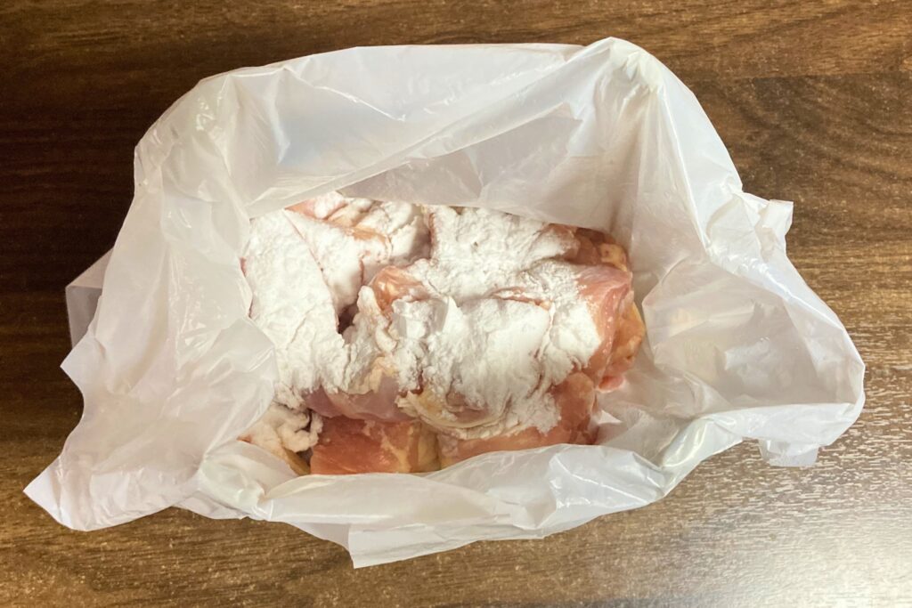 透明なポリ袋の中で片栗粉をまぶされている、一口大に切られた生の鶏肉。肉の旨味を閉じ込め、とろみをつけるための下準備の工程です。