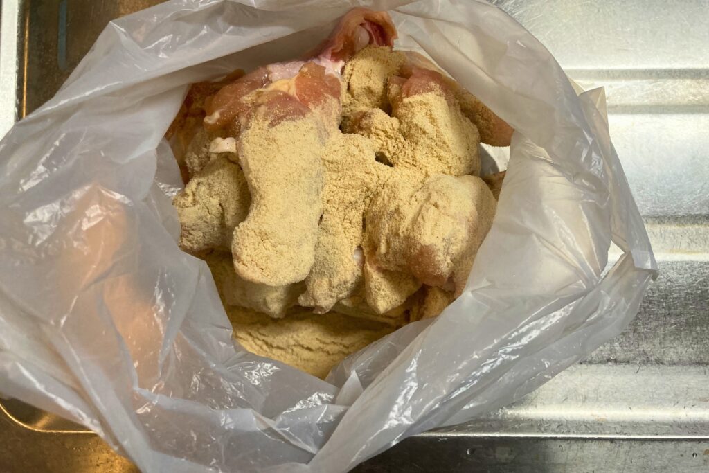 ビニール袋の中で生の鶏手羽元に唐揚げ粉などの衣となる粉末をまぶして下準備をしている様子。