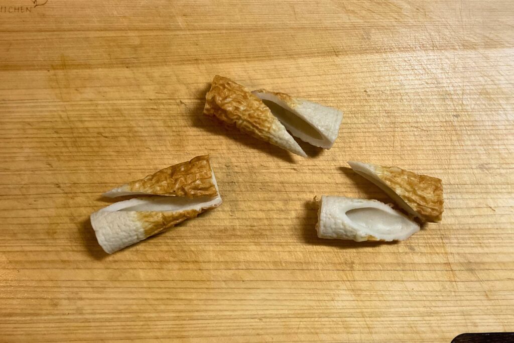 まな板の上に置かれた、斜めに半分に切り分けられた3本のちくわ。焼き色のついた表面と、中が空洞になった断面。