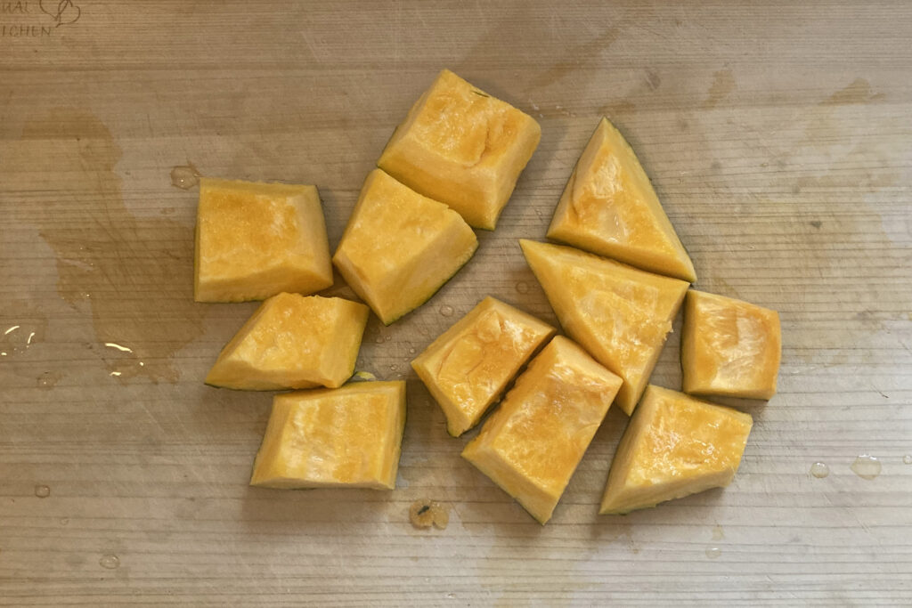 まな板の上に置かれた、一口大に乱切りされた生の黄色いかぼちゃ。