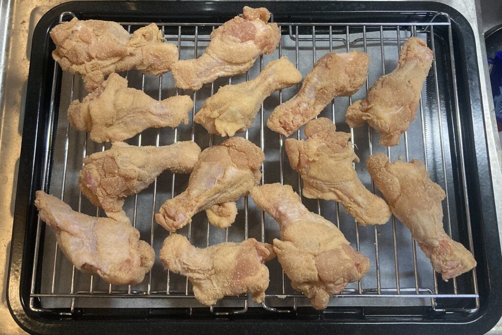 粉をまぶした鶏手羽元が、オーブン用の黒い角皿に乗せた金網の上に重ならないように等間隔で並べられている状態。
