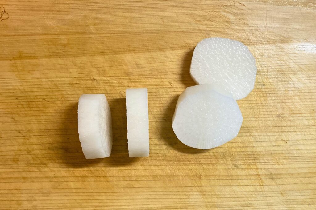 まな板の上に並べられた、厚さ3センチほどの輪切りにされた白い大根。皮を剥き、面取りを施した下準備済みの状態。