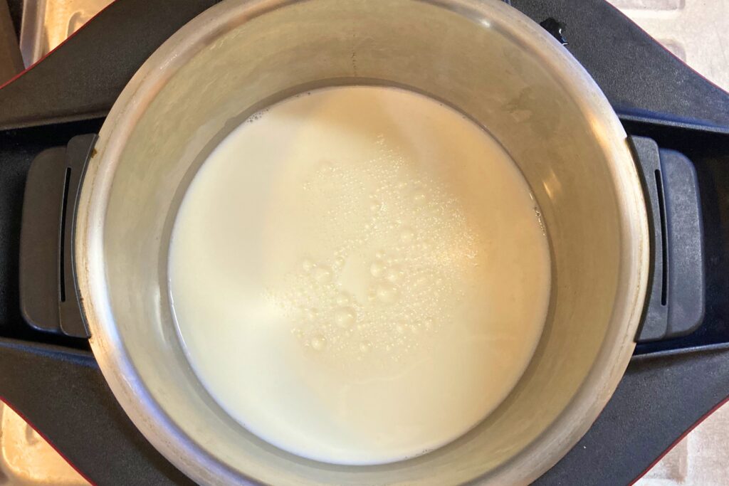 ホットクックの内鍋に牛乳を注いだ様子。白い液体が底に溜まり、表面には小さな気泡がわずかに浮かんでいる。