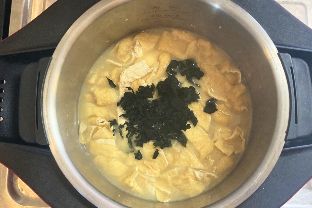 味噌を溶いた後の温かいお味噌汁の中に、中央に山盛りにされた乾燥わかめを後入れして、戻している調理の最終段階。