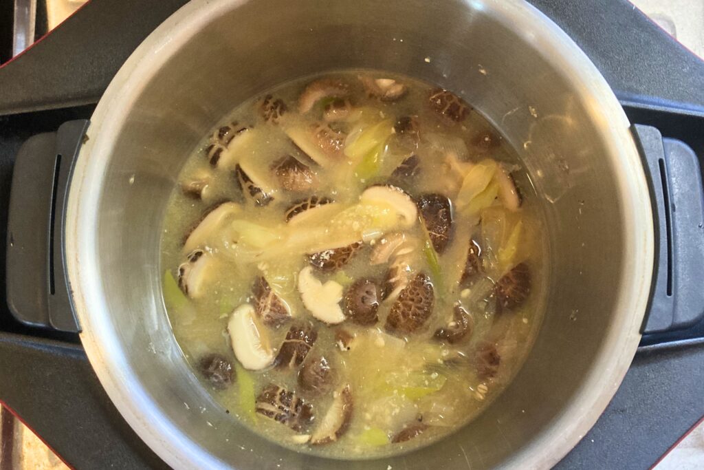 鍋の中でしいたけと長ねぎが柔らかく煮え、味噌が溶け合わされた状態。具材がスープに馴染み、湯気が立ちそうな調理完了直前の様子。