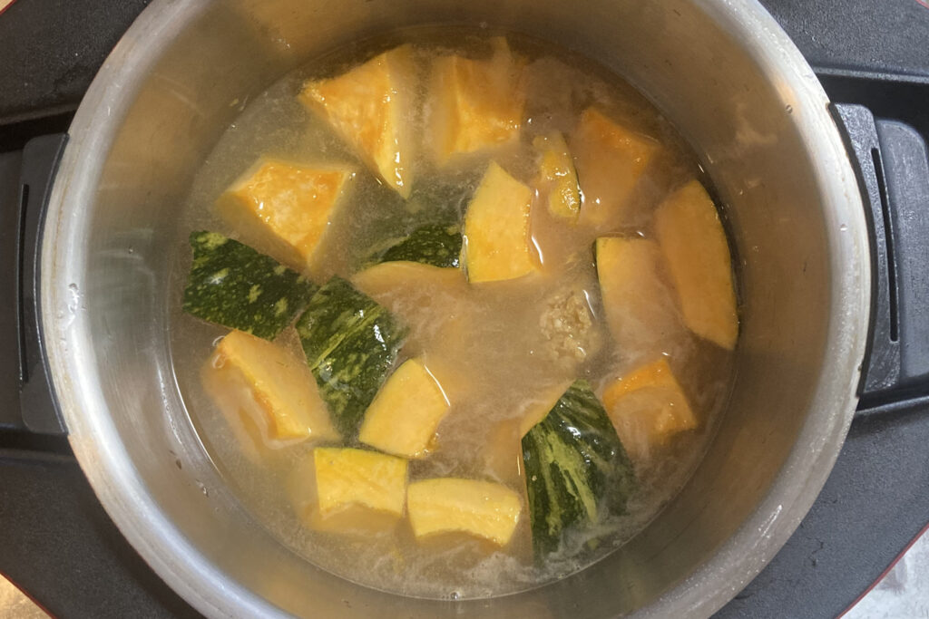 ホットクックのステンレス製の内鍋に、乱切りにしたかぼちゃと水が入っている様子。加熱前の状態。