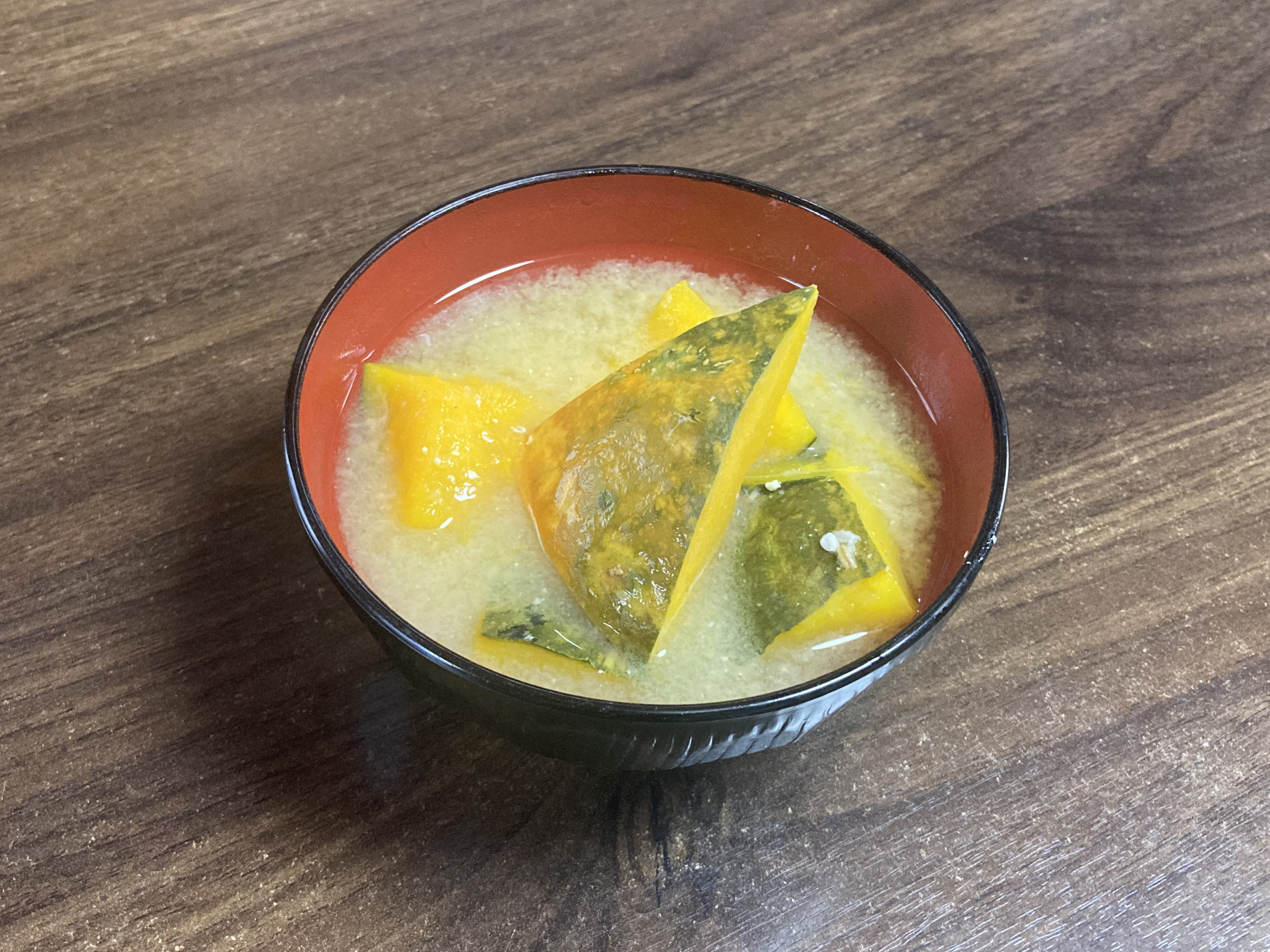 木目調のテーブルの上に置かれた、黒と朱色のお椀にたっぷりと盛られた完成したかぼちゃの味噌汁。