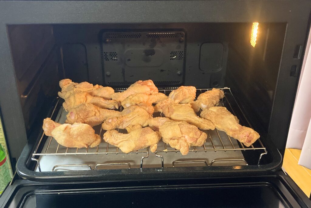 網の上に並べられた衣付きの鶏手羽元が、加熱される前の状態でオーブンレンジの庫内にセットされている様子。