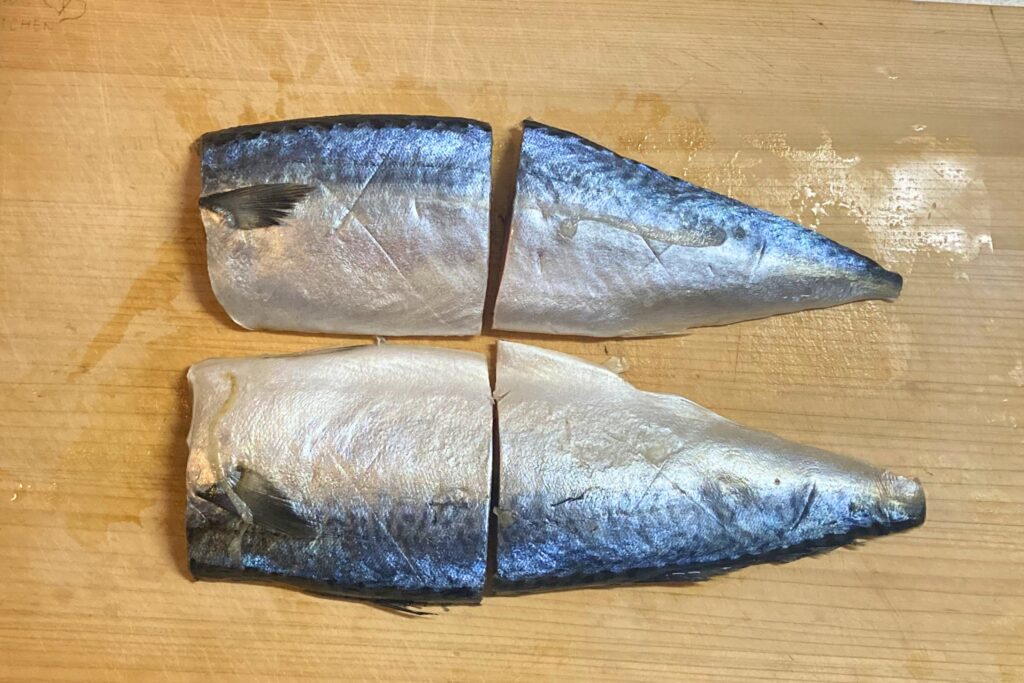 木のまな板の上に、生のサバの切り身が4切れ並んでいる。皮が上向きで、鮮やかな青色と網目模様が特徴。