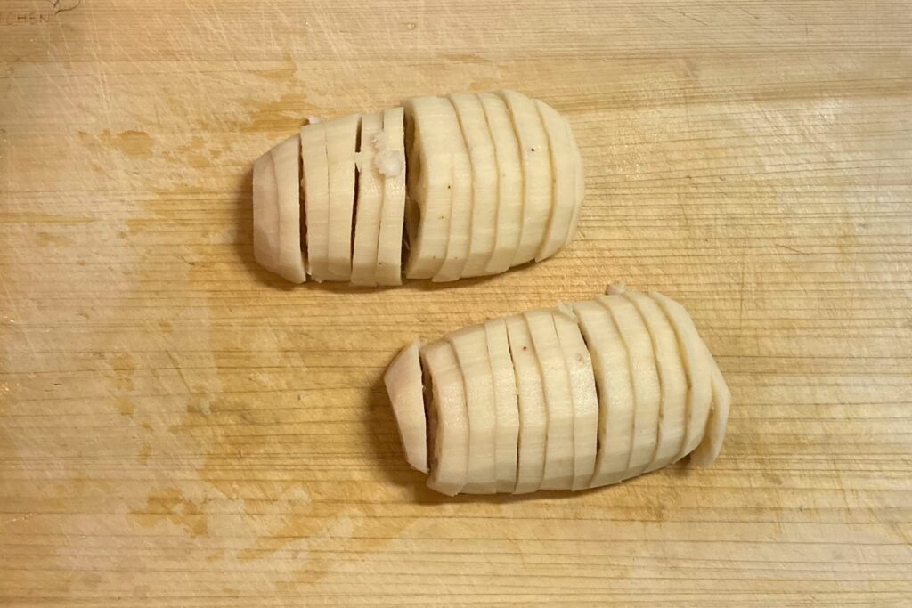 まな板の上で約1センチ幅の半月切りにされた2つの皮むきレンコン。料理の最初のステップである下ごしらえの様子を示しています。