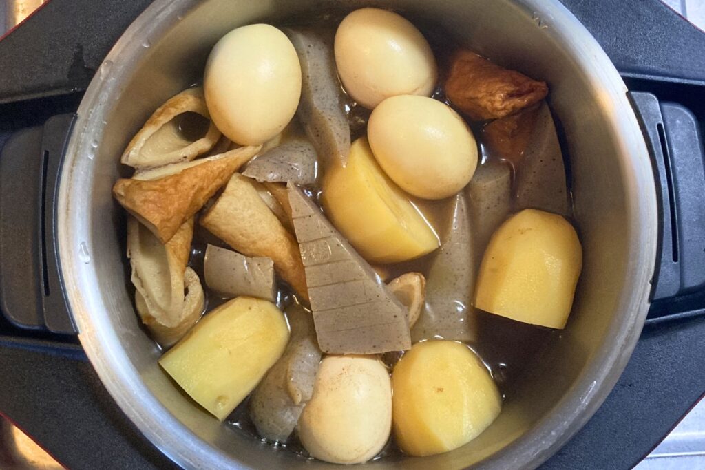 煮込みが進み、出汁の色が濃くなったおでん鍋。具材のゆで卵やちくわに出汁の色が少しずつ染み込んでいる様子。