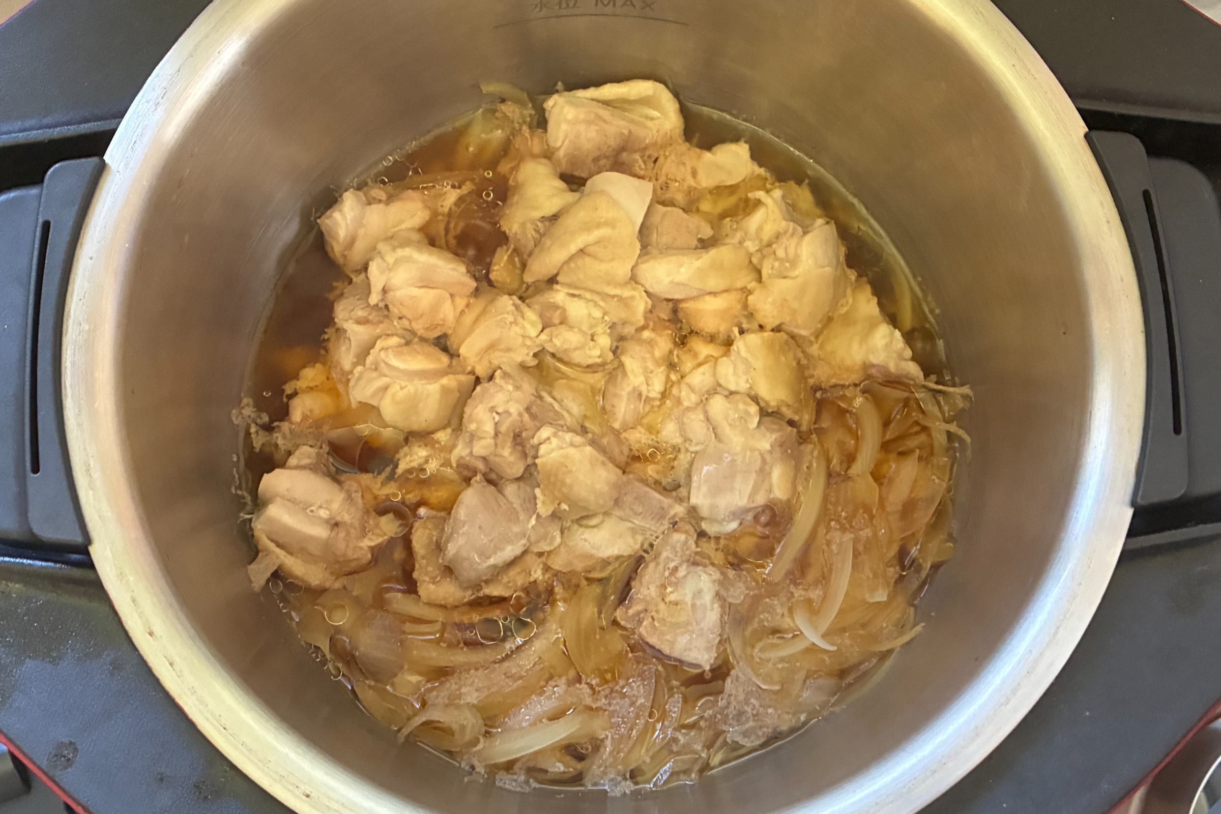ホットクックで12分間の加熱が終了してフタを開けた直後の内鍋。鶏もも肉と玉ねぎにしっかりと火が通り、底に琥珀色の煮汁がたっぷりと溜まっている状態。