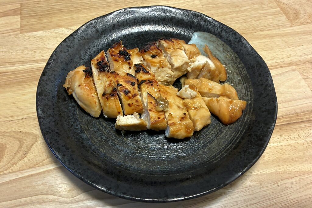 黒い丸皿に盛り付けた、そぎ切りの鶏むねステーキ。表面に焼き色がつき、断面は白くしっとりしている