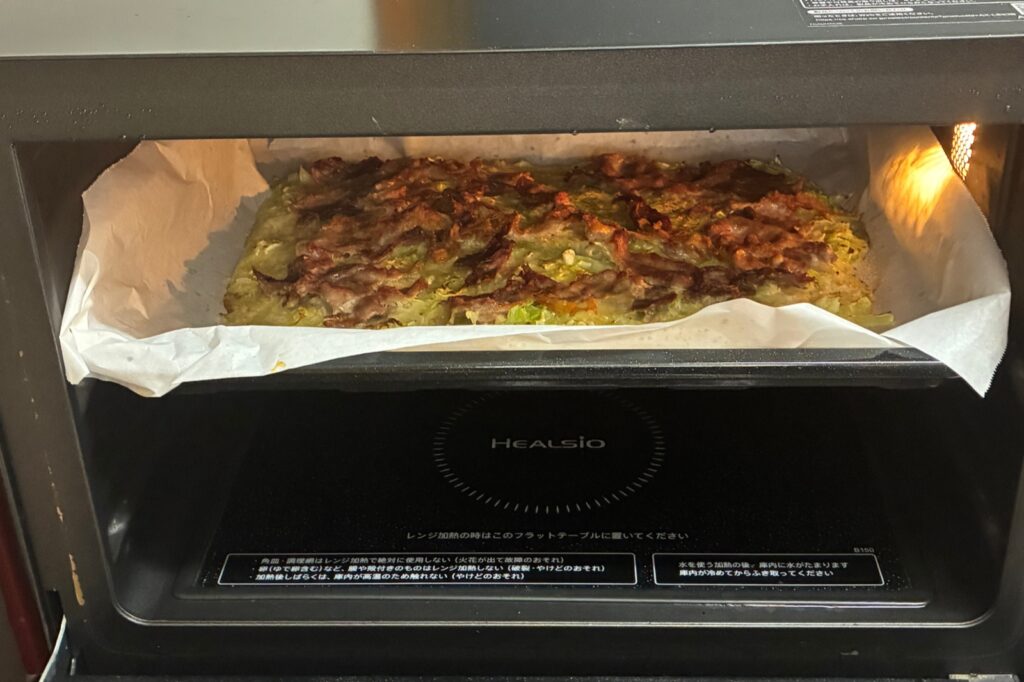 ヘルシオの扉を開けたところ。角皿の上で豚バラに焼き色がつき、お好み焼きが焼き上がっている