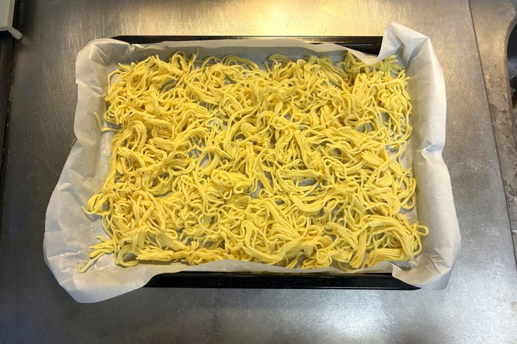 ヘルシオの角皿にクッキングシートを敷き、ほぐした焼きそば麺を重ならないように平らに広げた状態。