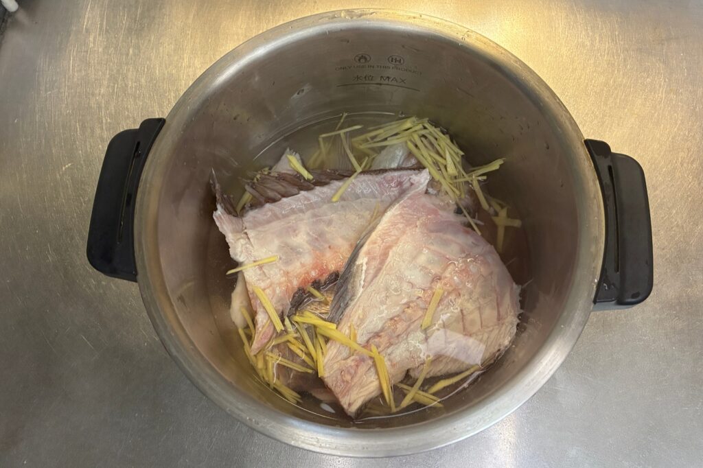 ホットクックの内鍋に鯛のあらと水を入れ、千切りの生姜を散らした状態。味噌はまだ入れていない