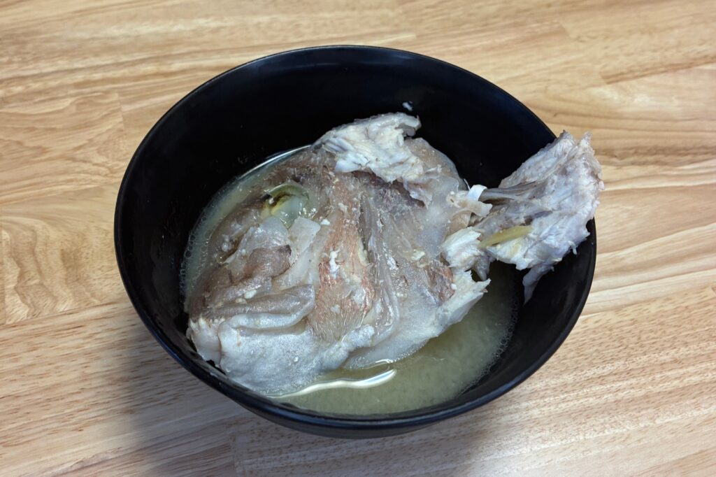 黒いお椀に盛った鯛のあらの味噌汁。頭と中骨が汁につかっている