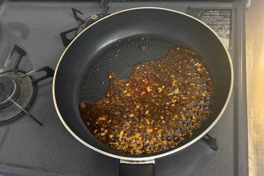 フライパンの中で醤油やみりん、酒、砂糖を煮詰め、表面にきめ細かい泡が立ってとろみがついてきた甘辛だれの様子。レバーを蒸している合間に手早く煮詰めて準備する。